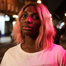 michaela coel in the tv show i may destroy you with pink hair and standing in the street