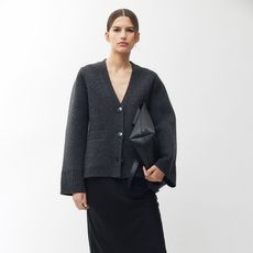 model wears gray structured cardigan, long black skirt, and oversized black