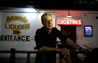 Anthony Bourdain leans over a railing outside of afomic liqours in Parts Unknown