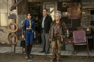 three people (Ella Purnell as Lucy MacLean, Michael Emerson as Wilzig, and Dale Dickey as Ma June) stand in front of a dilapidated store, in 'Fallout'