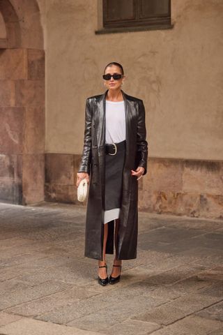 A woman wearing a leather maxi coat, white shirt, and gray skirt