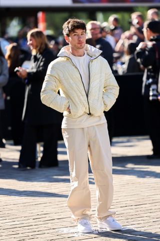 barry keoghan wears a ivory puffer jacket, ivory pants, a white t-shirt, and white sneakers.