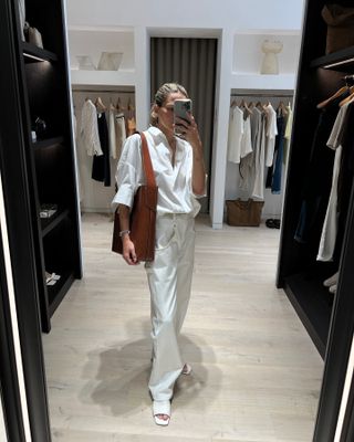 Eliza Huber wearing a white poplin collared shirt from Banana Republic with white carpenter jeans and an oversized brown bucket bag.