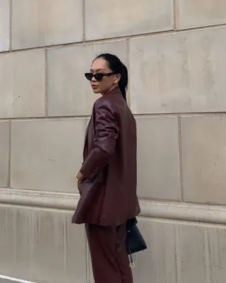 Woman wearing oxblood red suit, standing in front of wall taking outfit picture.