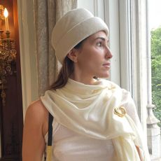 Editor Anna LaPlaca wearing white scarf, gold brooch, and white pillbox hat.