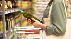 A shopper examines a bottle of olive oil in a supermarket