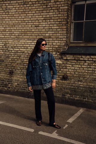 A woman wearing a blue denim jacket with studs and black pants.