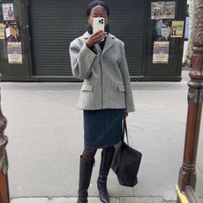 French fashion influencer Sylvie Mus taking a selfie on the street in Paris wearing a chic fall outfit with black knee-high boots.