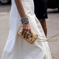 a street style image of a woman wearing a bracelet cuff and a gold handbag