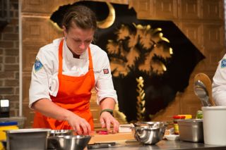 a chef in an orange apron cutting food on top chef