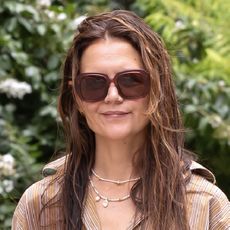 Katie Holmes is seen out and about on August 11, 2024 in New York, New York wearing a brown and white striped button-down shirt, a layer of beaded necklaces, and brown rectangular sunglasses.