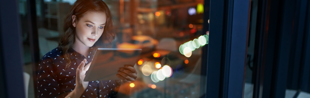 Woman standing in office window working on a tablet at night