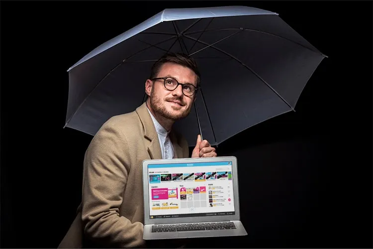 A man with a computer in his hand protects himself with an umbrella