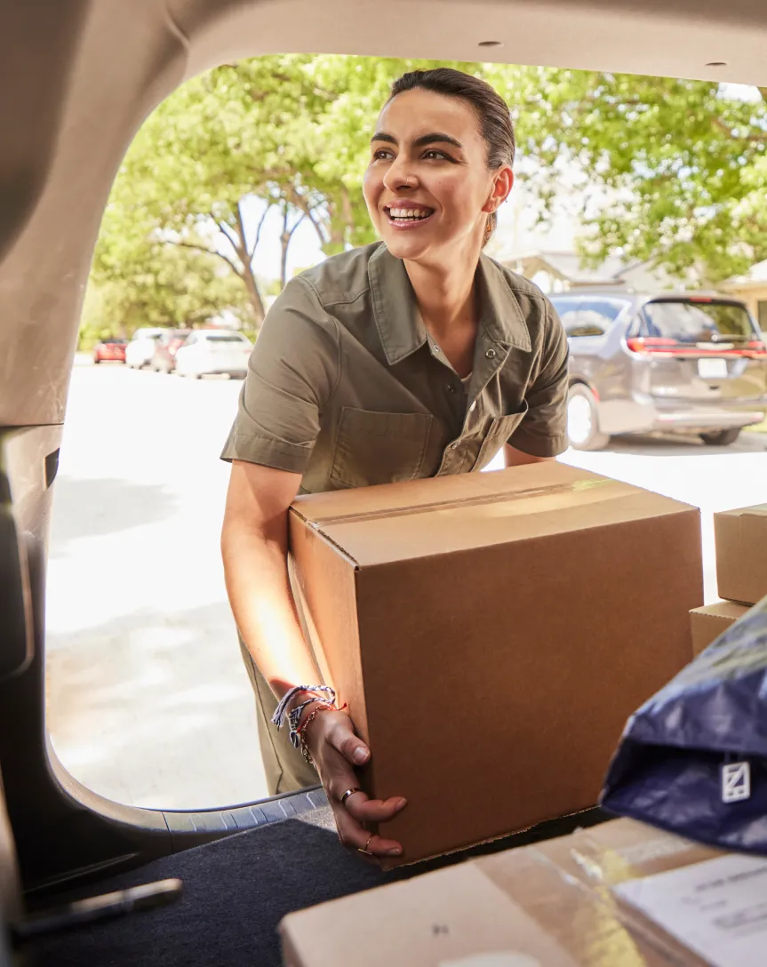 A woman Veho driver unloading a box from car's boot.