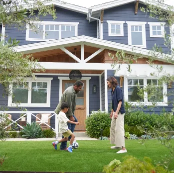 A man, woman and a kid, playing football in the lawn of their home.