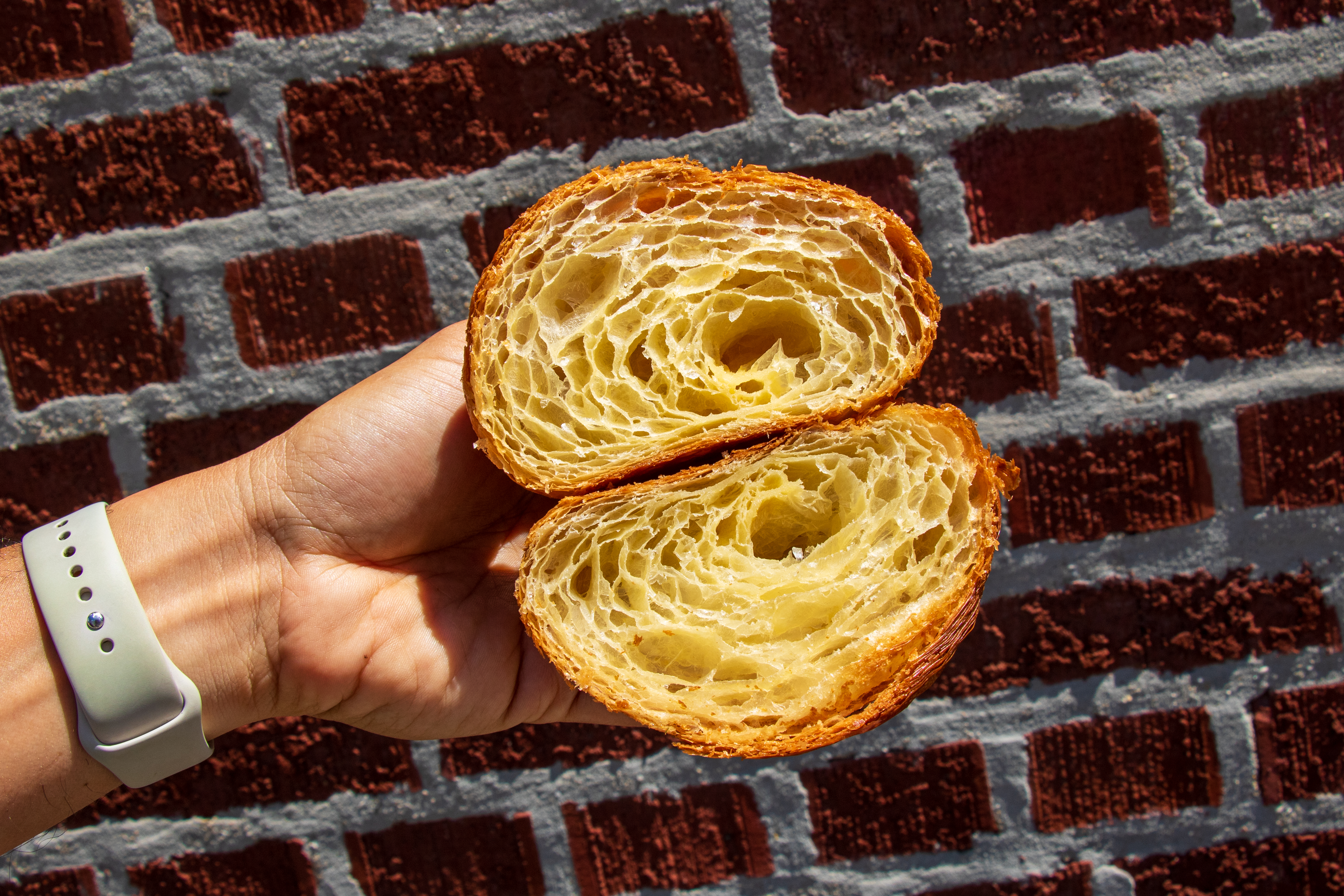 A hand holds a croissant that has been cut in half to expose a yellow cross-section.