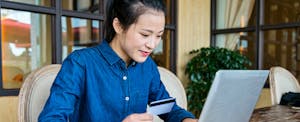 Young woman holding a credit card and using a laptop to find the 5 best Visa credit cards