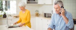 Senior man talking on mobile phone while woman washing plate in kitchen