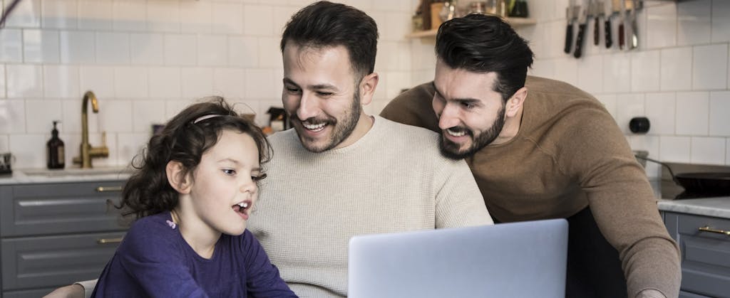 Happy fathers looking at daughter using laptop at table in kitchen