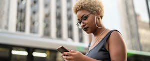 Woman in a city looking at her phone and reading about rebates on cars