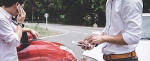 Two men standing next to their cars after getting into an accident, talking about insurance