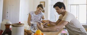 Couple in kitchen with cellphone, talking about how to transfer money from bank to bank