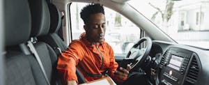 Young male driver using smart phone while sitting in delivery van.