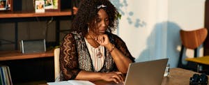 A woman seated at a table uses a laptop to look into getting her home appraised to help determine its fair market value.