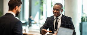 A man in a suit and tie uses his credit card while checking in at the front desk of a hotel.