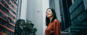 Young woman on a city street, looking up at big bank buildings around her.