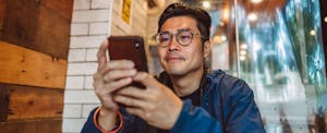 Young man sitting at a table in a cafe, reading on his phone