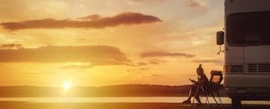 Distant view of a woman sitting near her camper van using with the sunset in the background