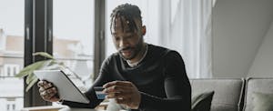 Man sitting at home on his couch, holding his credit card and reading about how to increase his Amex credit limit