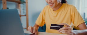 Young woman in front of her computer, with her credit card in hand, considering a Discover credit limit increase