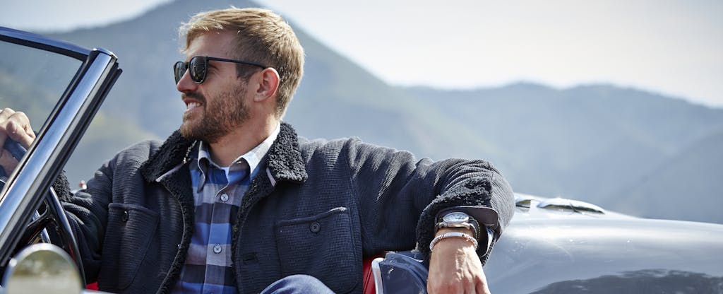 Man sitting in his classic car, enjoying the view while taking a break on his road trip