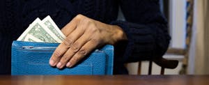 A closeup on a hand pulling several dollar bills out of a blue wallet