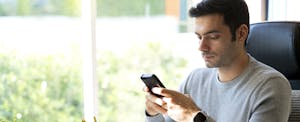 Man sitting in his office, using his mobile phone to check is Quontic checking account.