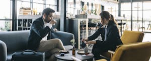 Two people seated with their luggage in an airport lounge, having tea and relaxing.