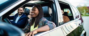 A smiling driver and their friends sitting in a car ready to depart for a road trip.