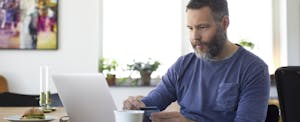 A person with a beard seated at a table using a laptop and holding their go2bank card.