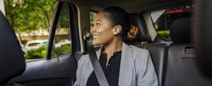 Professional woman sitting in the backseat of a car, looking out the window.