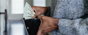 Close-up of someone's hands inserting twenty dollar bills into their wallet.