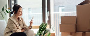 Young woman sits on couch looking at phone. Boxes are in front of her.