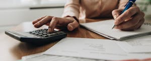 A close up photo of someone's hands using calculator while going through bills and home finances.