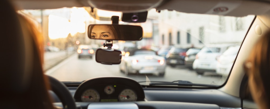 A woman drives a car with a passenger in the backseat.