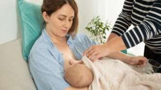 A woman breastfeeding while a consultant assists. | Oksix | Dreamstime.com