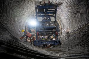 people in protective gear in large tunnel with heavy equipment