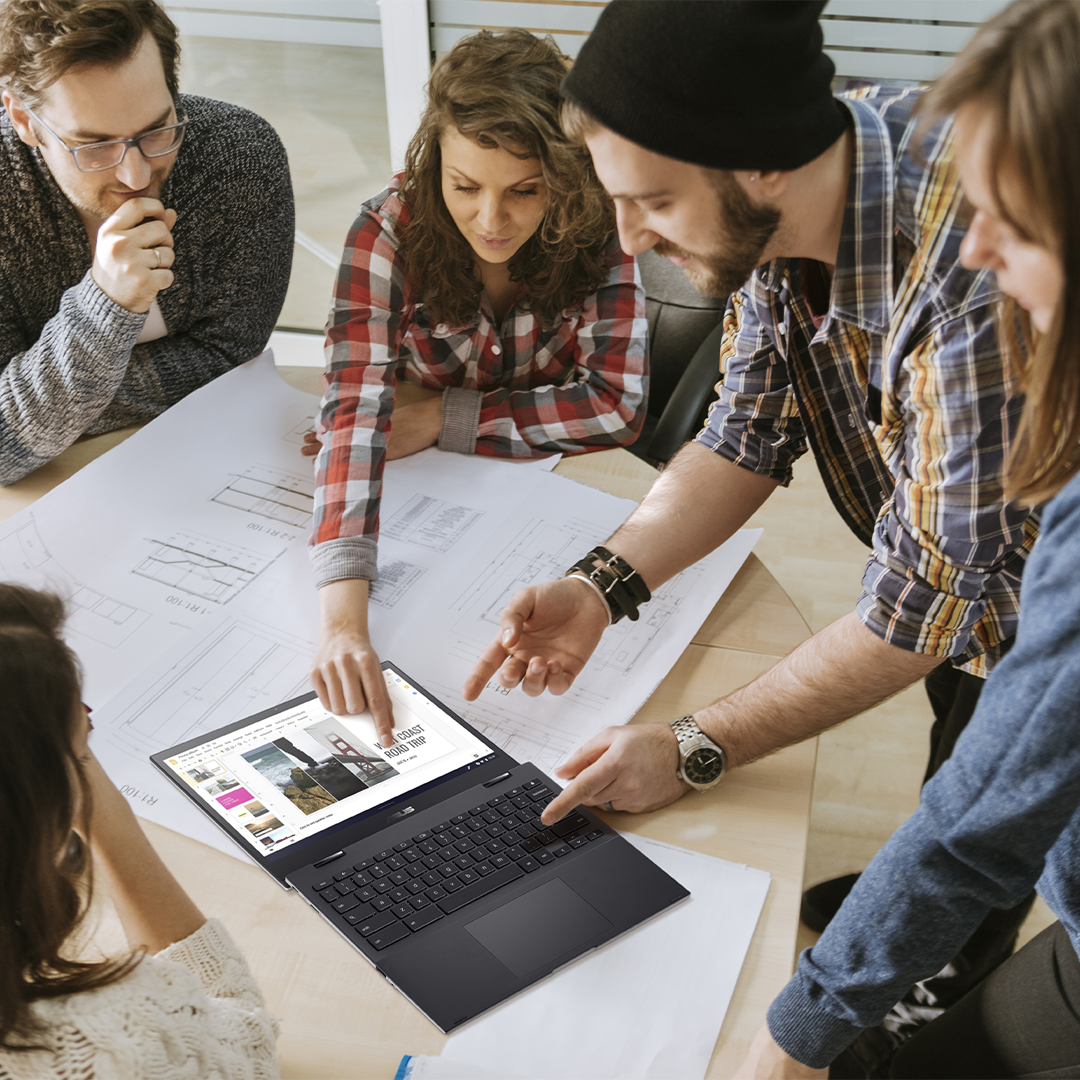 A group of youth is discussing together, looking at a ASUS Chromebook open in 180 degree flat on the desk.