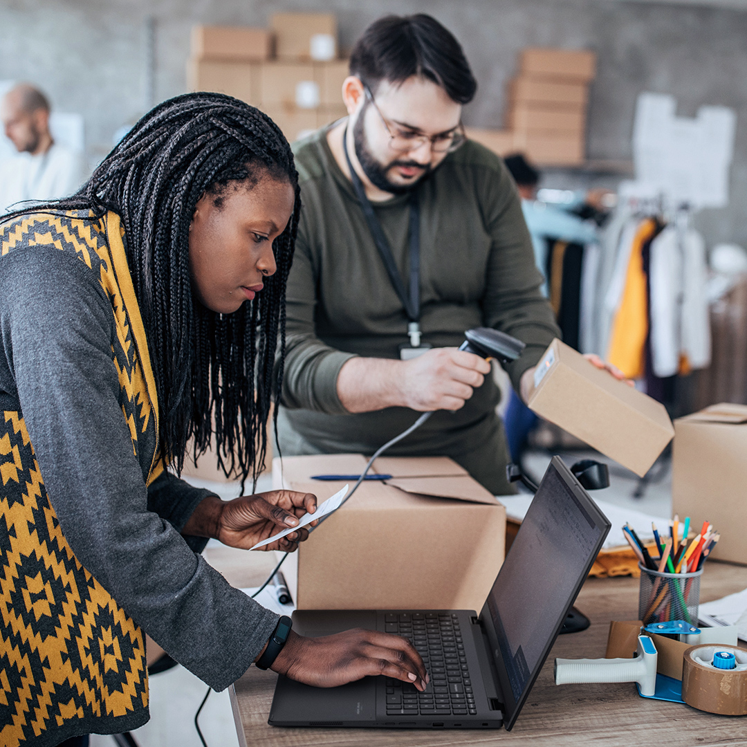 One cloth e-shop staff is checking information on an ASUS Chromebook and another staff is scanning barcode on the package box.