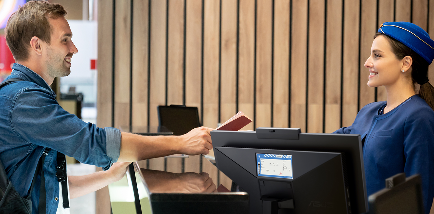 A traveler is checking-in at the front desk of a hotel. There is an ASUS ExpertCenter AiO at the front desk. 